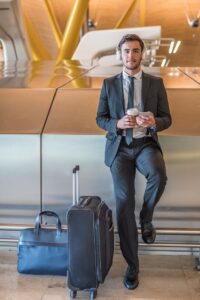 businessman at the airport listening music using his mobile phone waiting his flight with luggage